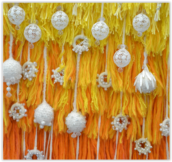 keltaisen sävyjä ja valkoisia koristeita tekstiilitaideteoksessa