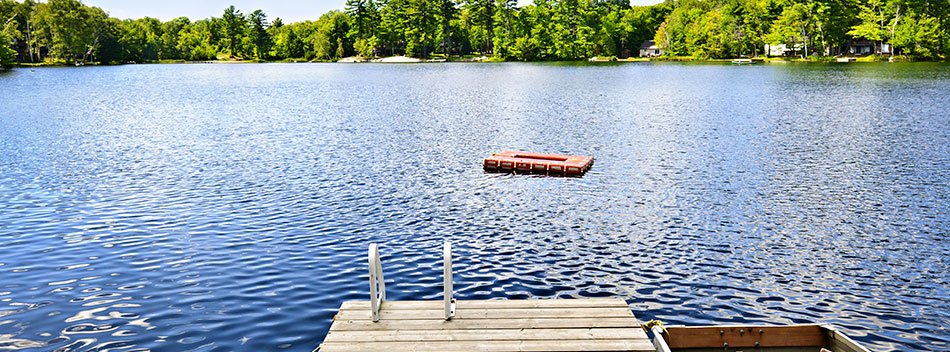 a picture of pier and a lake, surrounded by houses and forest